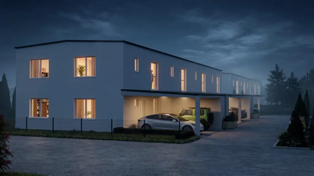 Nachtansicht des Wohnprojekts Reihenweise Grün mit beleuchteten Fenstern, Carports und Zufahrt